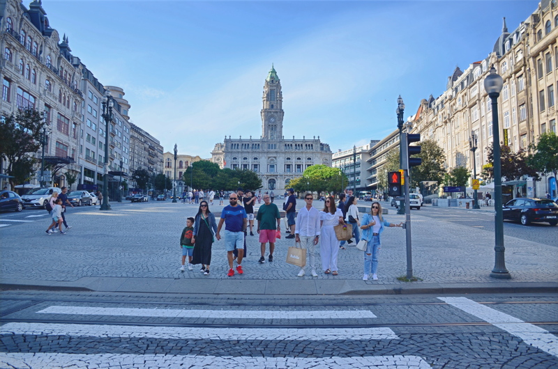 1 - A family and pedestrians walking across the grand Avenida dos Aliados in Porto, Portugal, with the iconic Porto City Hall rising in the background